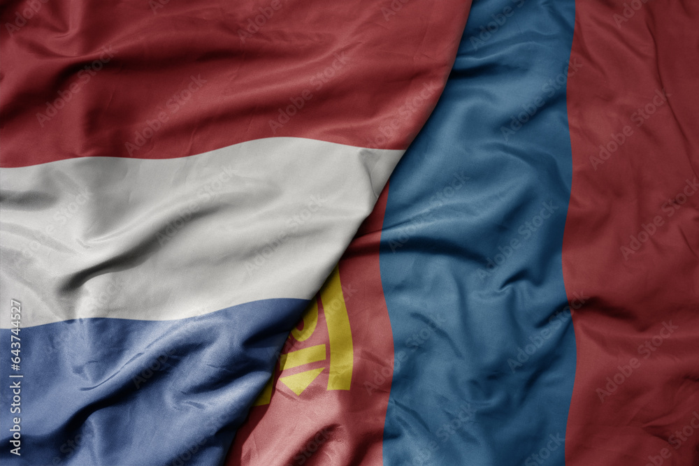 big waving national colorful flag of netherlands and national flag of mongolia .