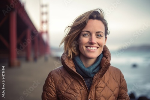 Environmental portrait photography of a grinning girl in her 30s wearing a quilted insulated jacket at the golden gate bridge in san francisco usa. With generative AI technology © Markus Schröder