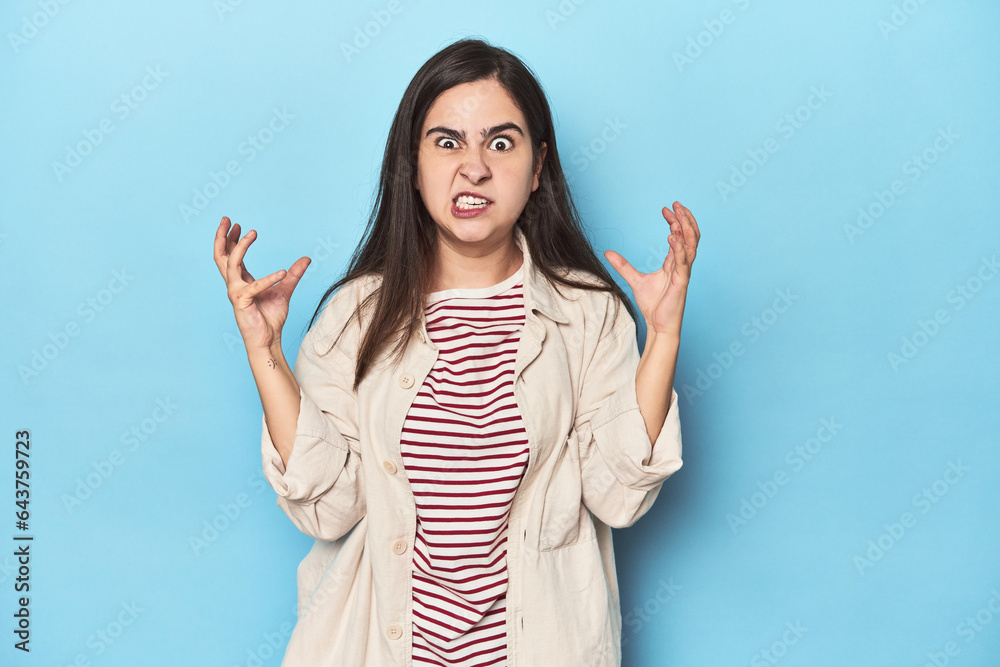 Young Caucasian woman on blue backdrop screaming with rage. Young Caucasian woman on blue backdrop screaming with rage.