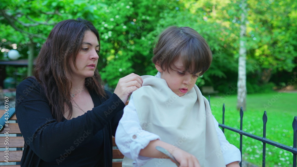 Mother putting napkin on child's collar to protect clothes from stains during lunch meal time. Authentic motherhood concept, smudge prevention Mother putting napkin on child's collar to protect clothes from stains during lunch meal time. Authentic motherhood concept, smudge prevention