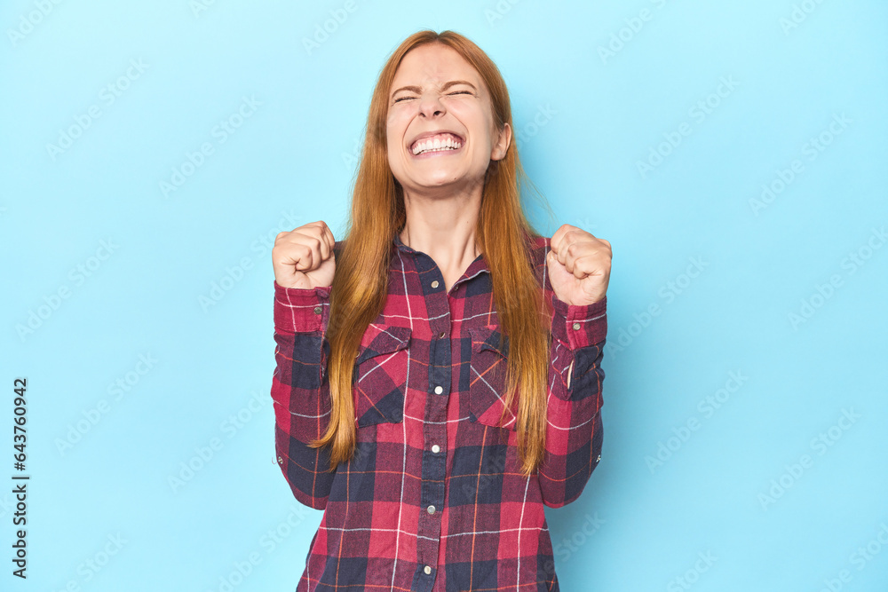 Redhead young woman on blue background celebrating a victory, passion and enthusiasm, happy expression. Redhead young woman on blue background celebrating a victory, passion and enthusiasm, happy expression.