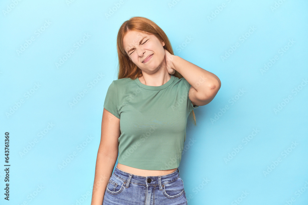 Redhead young woman on blue background suffering neck pain due to sedentary lifestyle. Redhead young woman on blue background suffering neck pain due to sedentary lifestyle.
