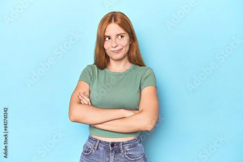 Redhead young woman on blue background dreaming of achieving goals and purposes
