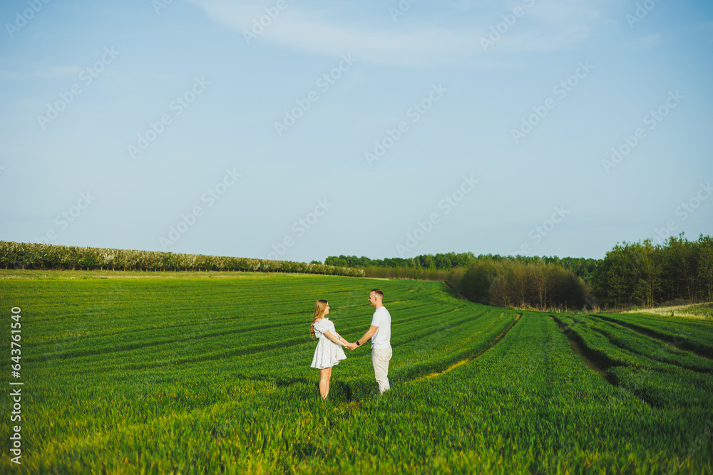 Pregnant couple hugging in a green spring field. Expectant parents in the park of white flowering trees. A romantic couple expecting a baby. A walk through a green field