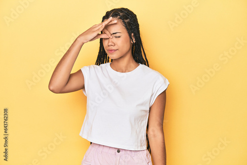 Young Indonesian woman on yellow studio backdrop having a head ache, touching front of the face.