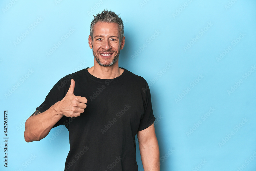 Middle-aged caucasian man on blue backdrop smiling and raising thumb up Middle-aged caucasian man on blue backdrop smiling and raising thumb up