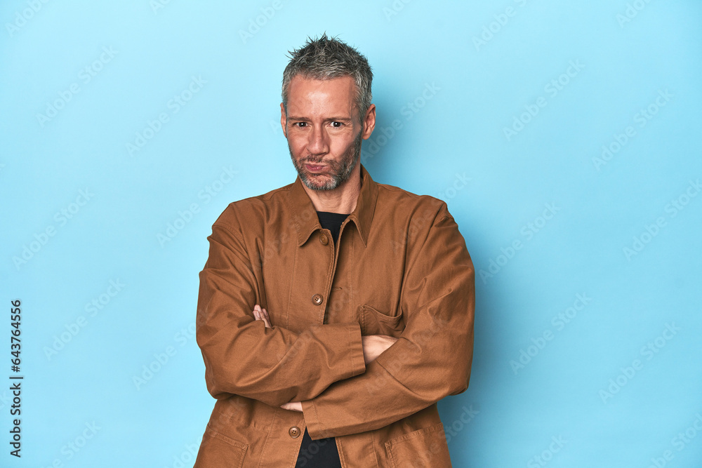 Middle-aged caucasian man on blue backdrop suspicious, uncertain, examining you. Middle-aged caucasian man on blue backdrop suspicious, uncertain, examining you.