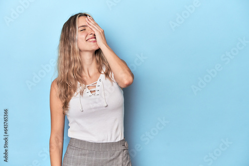 Blonde young caucasian woman in blue studio laughing happy, carefree, natural emotion.