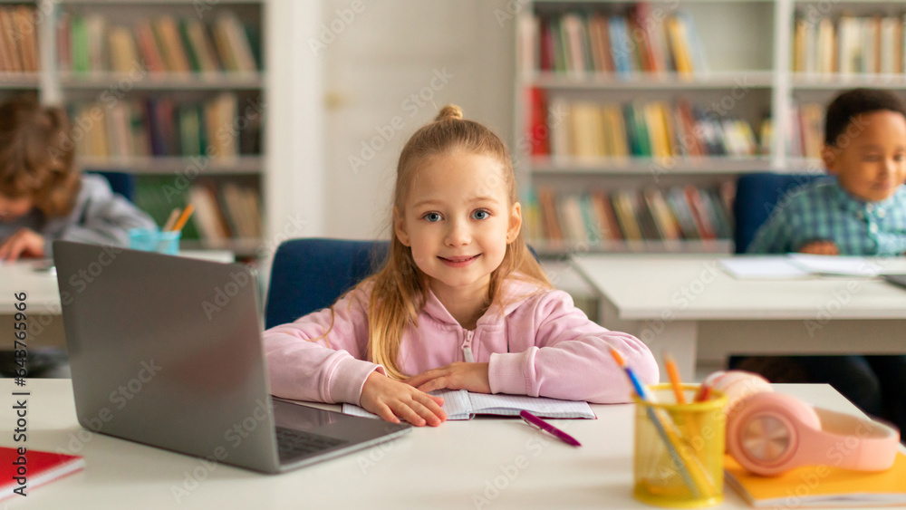 Happy caucasian school girl using laptop at class, looking and smiling at camera, using technology during tech lesson Happy caucasian school girl using laptop at class, looking and smiling at camera, using technology during tech lesson