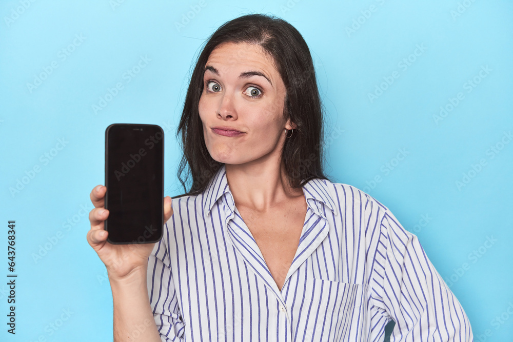Woman displaying phone screen on blue backdrop Woman displaying phone screen on blue backdrop