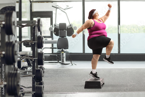 Full length profile shot of an overweight woman exercising step aerobics in a gym