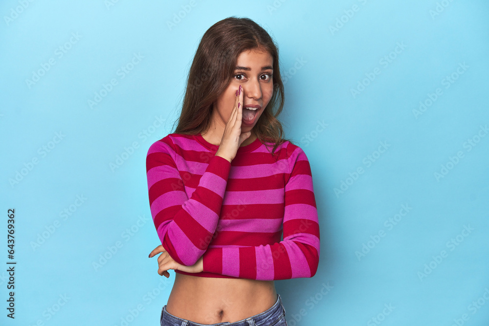 Teen girl in striped pink and red tee on blue saying a gossip, pointing to side reporting something. Teen girl in striped pink and red tee on blue saying a gossip, pointing to side reporting something.