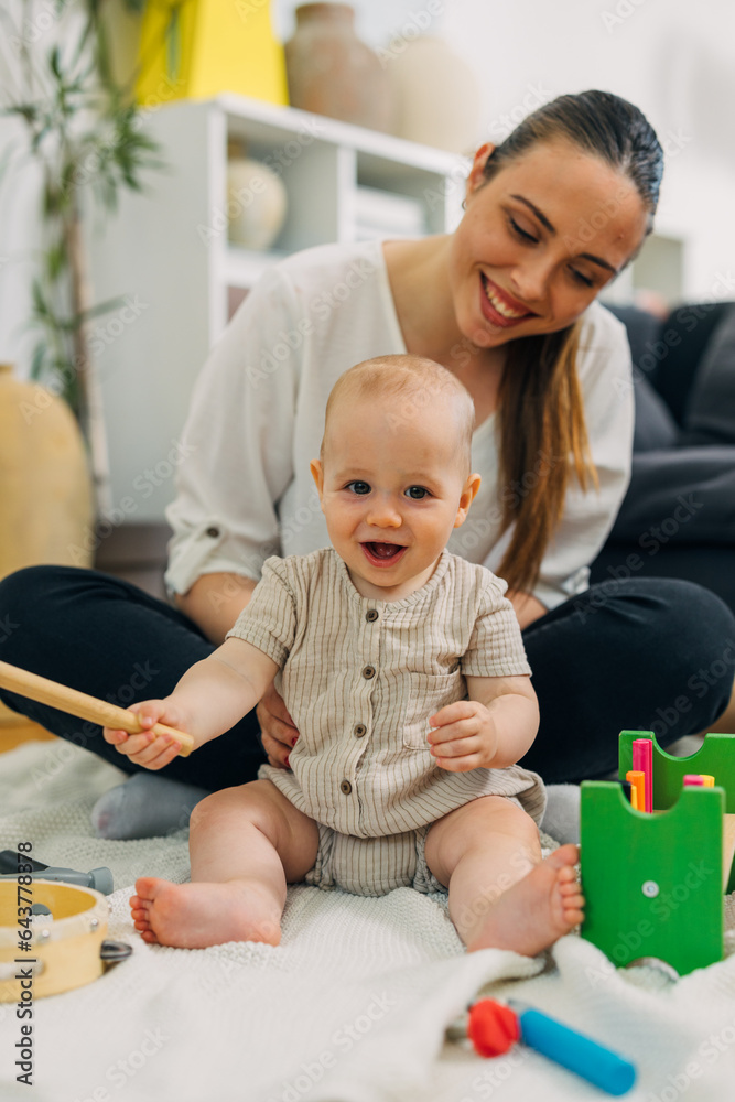 Happy baby plays with wooden toys with a help of a beautiful happy mother.