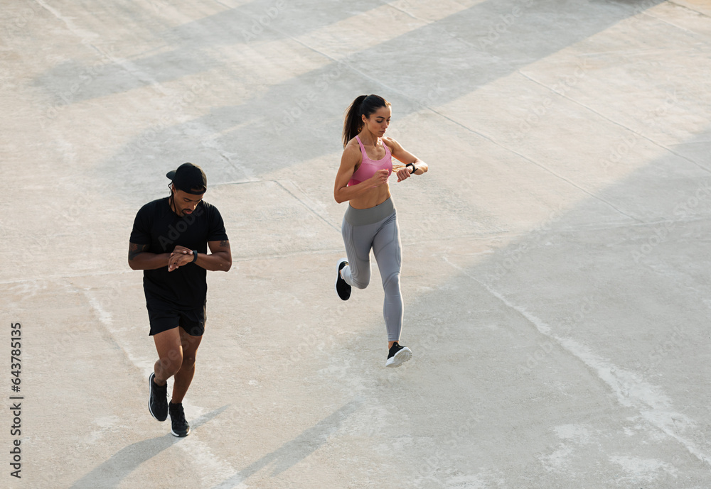 Two athletes checking their smartwatches during a run on the roof