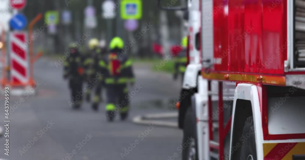 Group of fire men in uniform during blaze, fire fighting operation in the city streets, firefighters with the fire engine truck fighting vehicle in the background, emergency and rescue, slow motion Group of fire men in uniform during blaze, fire fighting operation in the city streets, firefighters with the fire engine truck fighting vehicle in the background, emergency and rescue, slow motion