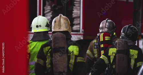 Group of fire men in uniform during blaze, fire fighting operation in the city streets, firefighters with the fire engine truck fighting vehicle in the background, emergency and rescue, slow motion