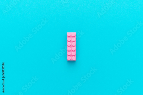 Central composition of plastic building block on turquoise blue background with copy space. Minimalist flat lay image of one pink constructor block.