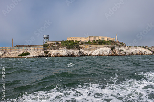 San Francisco, CA, USA - July 12, 2023: Alcatraz Island NW tip with tall chimney and new industries building, Water tower and lighthouse. White guano covered rocky cliffs under light blue sky