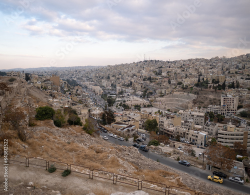Cityscape of Amman, as seen from the Amman Citadel. Houses are built over the sloping hillside, in the center of which is the ruin of the enormous Roman Theatre, showing a mix of old and new elements.