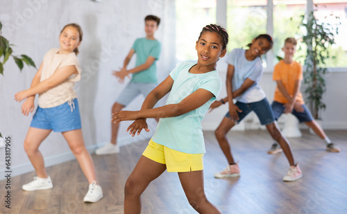 Positive juvenile girl engaged in Breakdancing together with children's group in training room during workout session