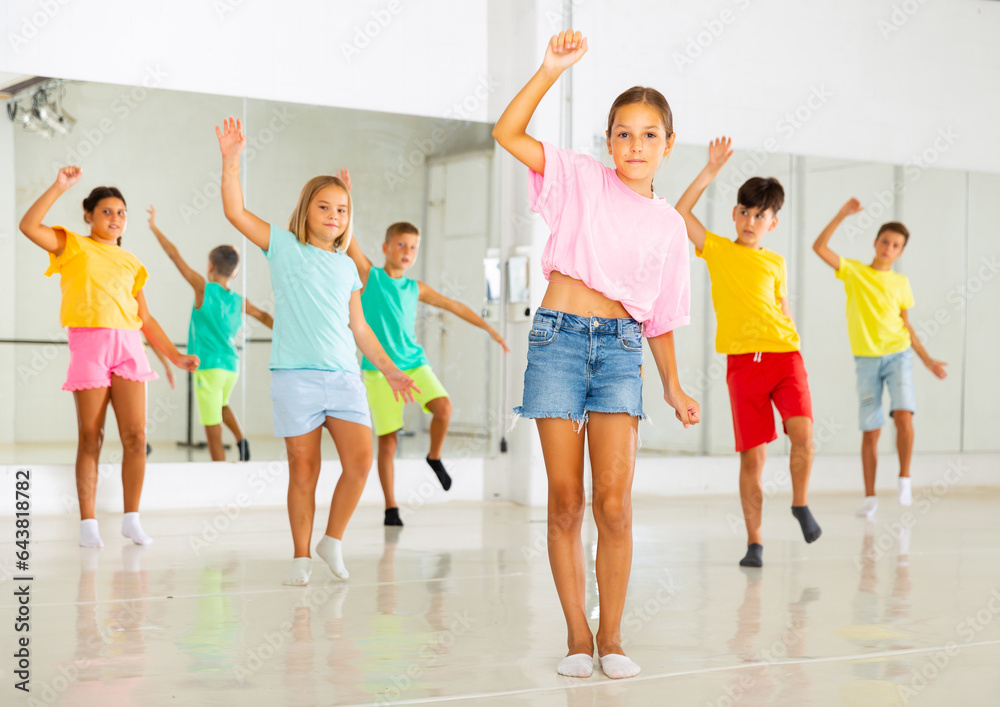 Obraz premium Portrait of cheerful preteen girl learning energetic dance moves with group of children in choreography class .