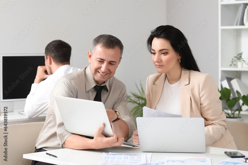 Business consultants working with laptop at table in office Business consultants working with laptop at table in office