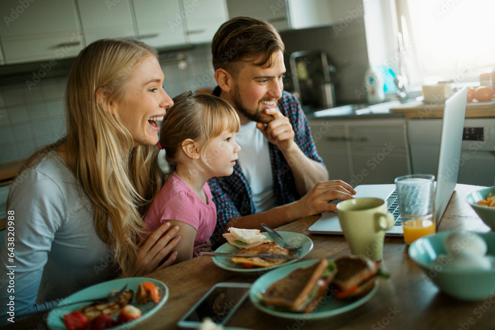 Young family having breakfast and using a laptop in the kitchen at home Young family having breakfast and using a laptop in the kitchen at home