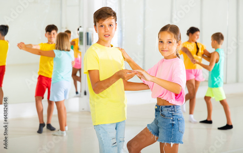 Portrait of positive tweenagers practicing slow ballroom dances in pairs in choreographic studio.