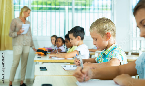 Group of focused pupils sitting at classroom working at class with teacher