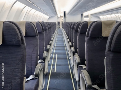 Inside passenger airplane - aisle and rows of seats, all in shades of grey colour. Empty