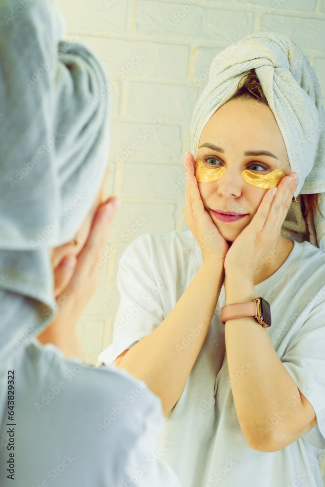 Beautiful woman applying collagen patches under eyes in front of the mirror.
