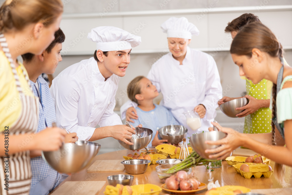 ..Young guy and adult woman chef at master class teaches group of children how to cook food