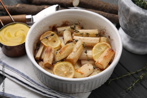 Dish with baked salsify roots, lemon and thyme on black wooden table