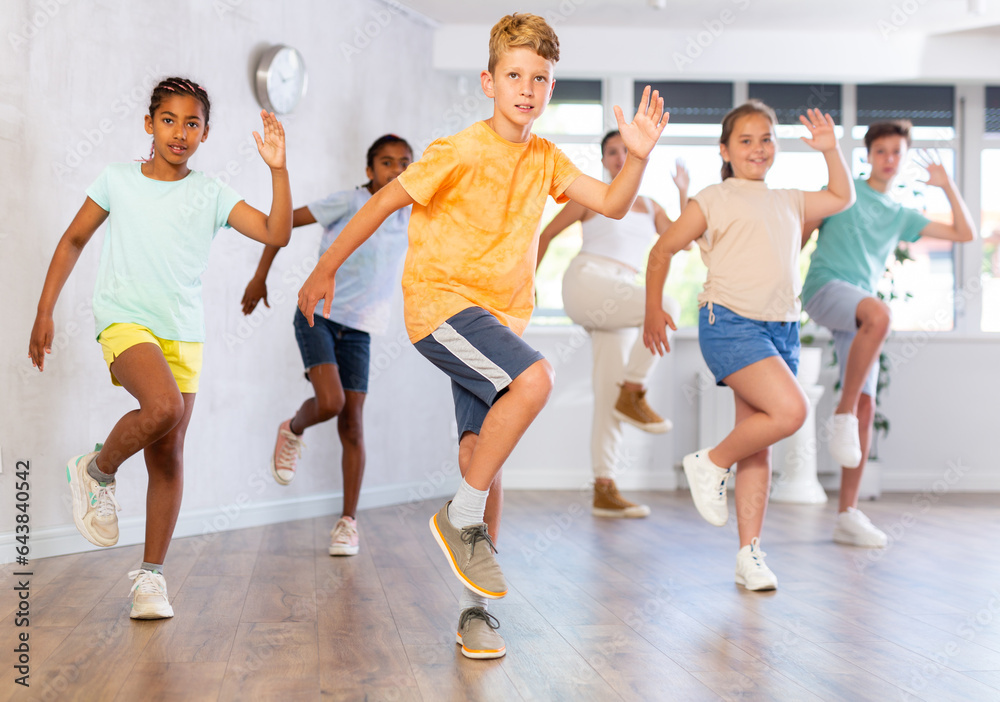 Positive male child dances vogue in choreographic school. Group of young people in sportswear trains together with classmates in gym before competitions, teacher takes part in class in background