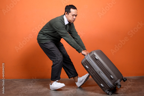 Traveler guy with big heavy luggage on orange background