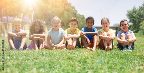 Happy team of friends children resting on grass at sunny day in park © JackF