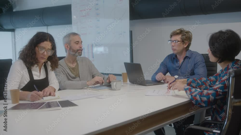 Mid-aged CEO holding business meeting in the office, sitting with mature colleagues around the table, looking through papers and discussing company strategy Mid-aged CEO holding business meeting in the office, sitting with mature colleagues around the table, looking through papers and discussing company strategy