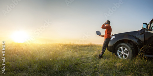  businessman doing remote business near his car at the meadow with computer. bannert with copy space.