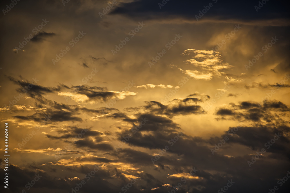 Sun casting long shadows and warm golden hue over clouds