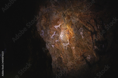 Figure animals and image of god Tengri on the stone wall of the cave, drawings ancient prehistoric people.