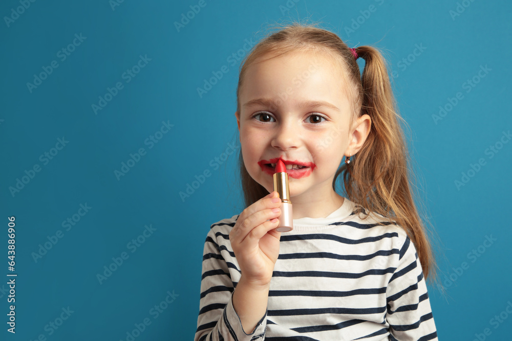 Happy little girl puts lipstick on her lips on blue background. Little trendy. little girl applying makeup Happy little girl puts lipstick on her lips on blue background. Little trendy. little girl applying makeup
