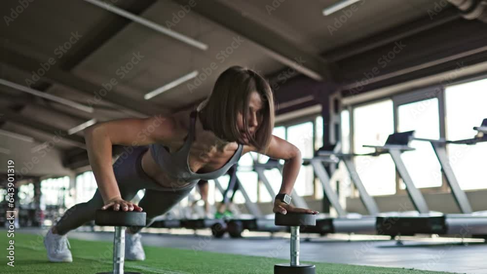 In the well-equipped gym, a sporty woman lifts dumbbells as part of her training. Focused Workout Sporty Woman Lifts Dumbbells in Gym Training