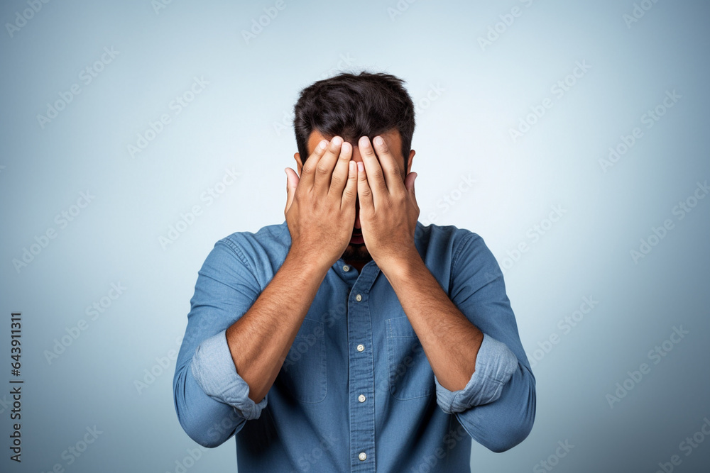 A man covering his face with his hands in front of a blue background, Generative AI A man covering his face with his hands in front of a blue background, Generative AI