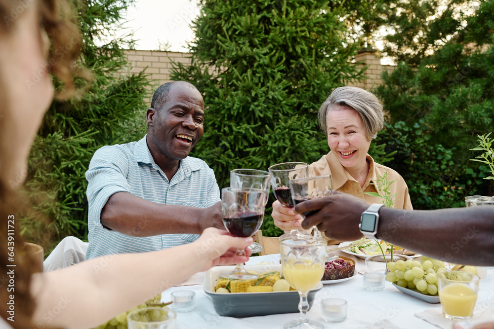 Happy mature intercultural couple with glasses of homemade red wine toasting with their son and his wife over table served for dinner Happy mature intercultural couple with glasses of homemade red wine toasting with their son and his wife over table served for dinner
