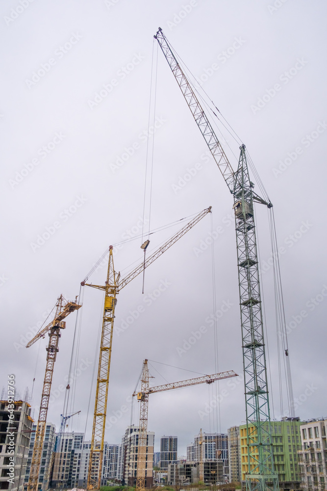 A crane and a building under construction against a blue sky background. Builders work on large construction sites, and there are many cranes working in the field of new construction.