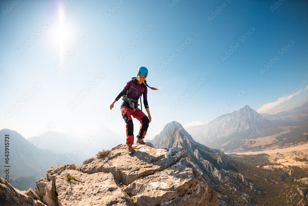 young girl climber in a helmet and with a backpack walks along a mountain range against the backdrop of mountains and climbing and hiking.