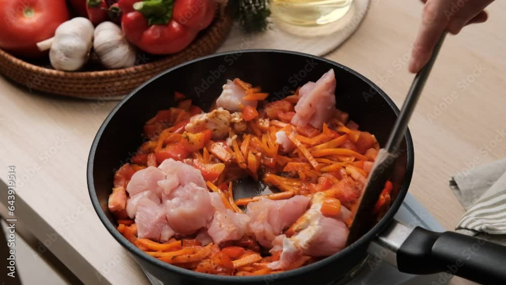 Close-up of a woman frying chicken fillet with vegetables and spices in a pan. Concept of domestic lifestyle. Cooking healthy food at home Close-up of a woman frying chicken fillet with vegetables and spices in a pan. Concept of domestic lifestyle. Cooking healthy food at home
