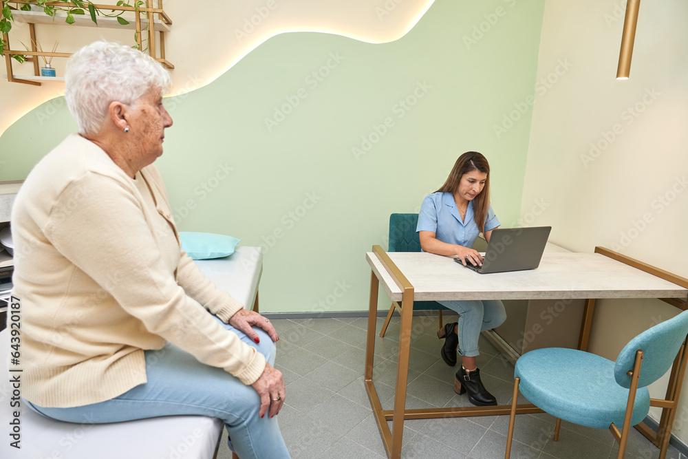 Obraz premium Doctor using laptop next to a old patient