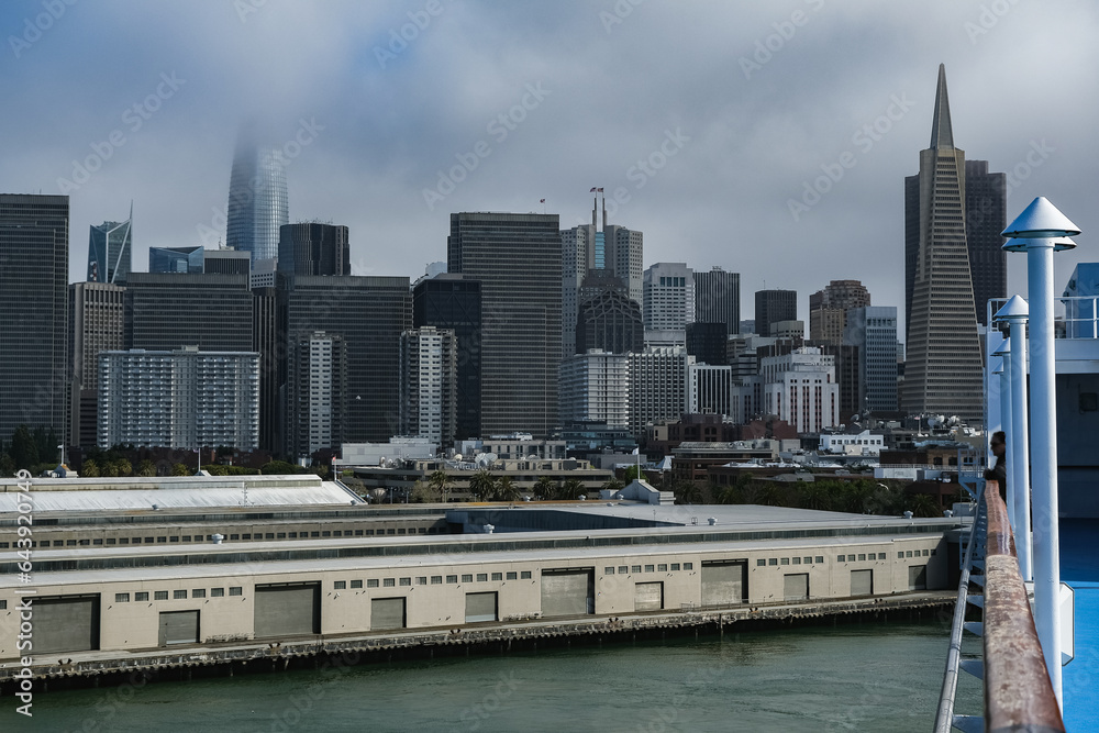 Grey foggy low hanging clouds day in San Francisco Bay with port piers, city skyline downtown architecture highrise buildings and landmarks as Coit Tower or Pyramid