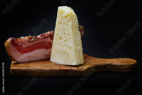 Vászonkép bacon and pecorino romano on a wooden chopping board with a black background
